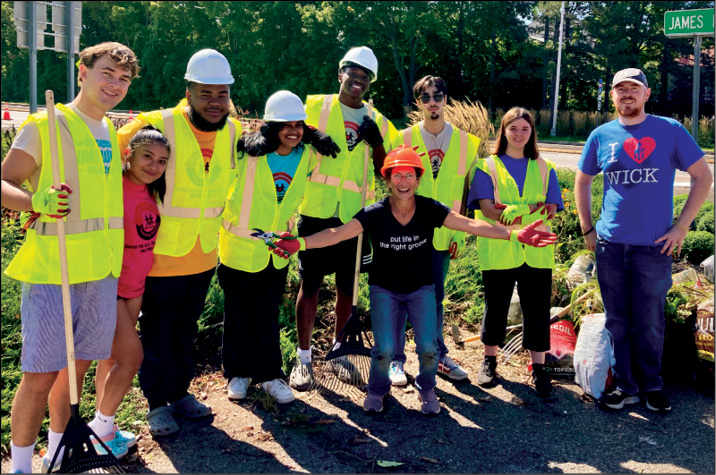 Volunteers in hard hats and safety vests working together along a roadside in Oneonta